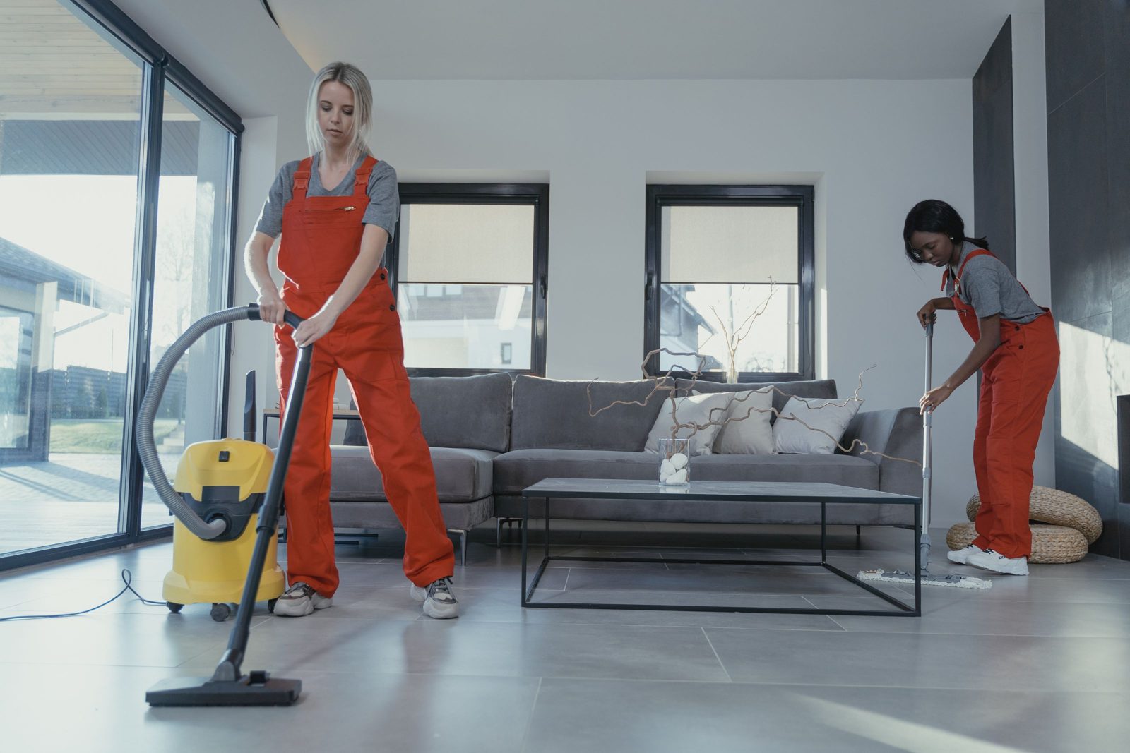 Due addette in tuta da lavoro puliscono un soggiorno